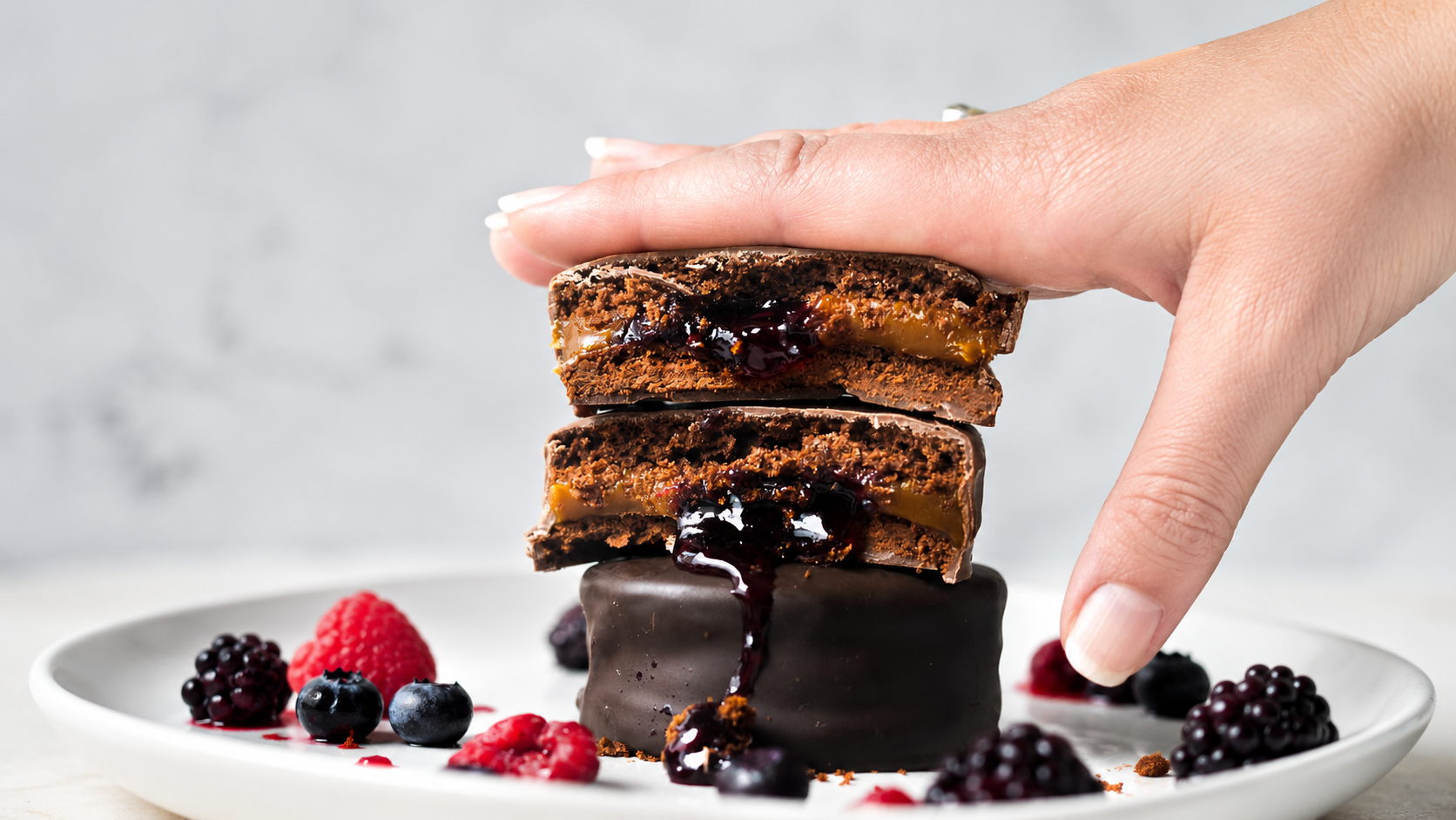 Alfajores de chocolate con dulce de leche y mermelada de frutos rojos sobre un plato con frutos del bosque